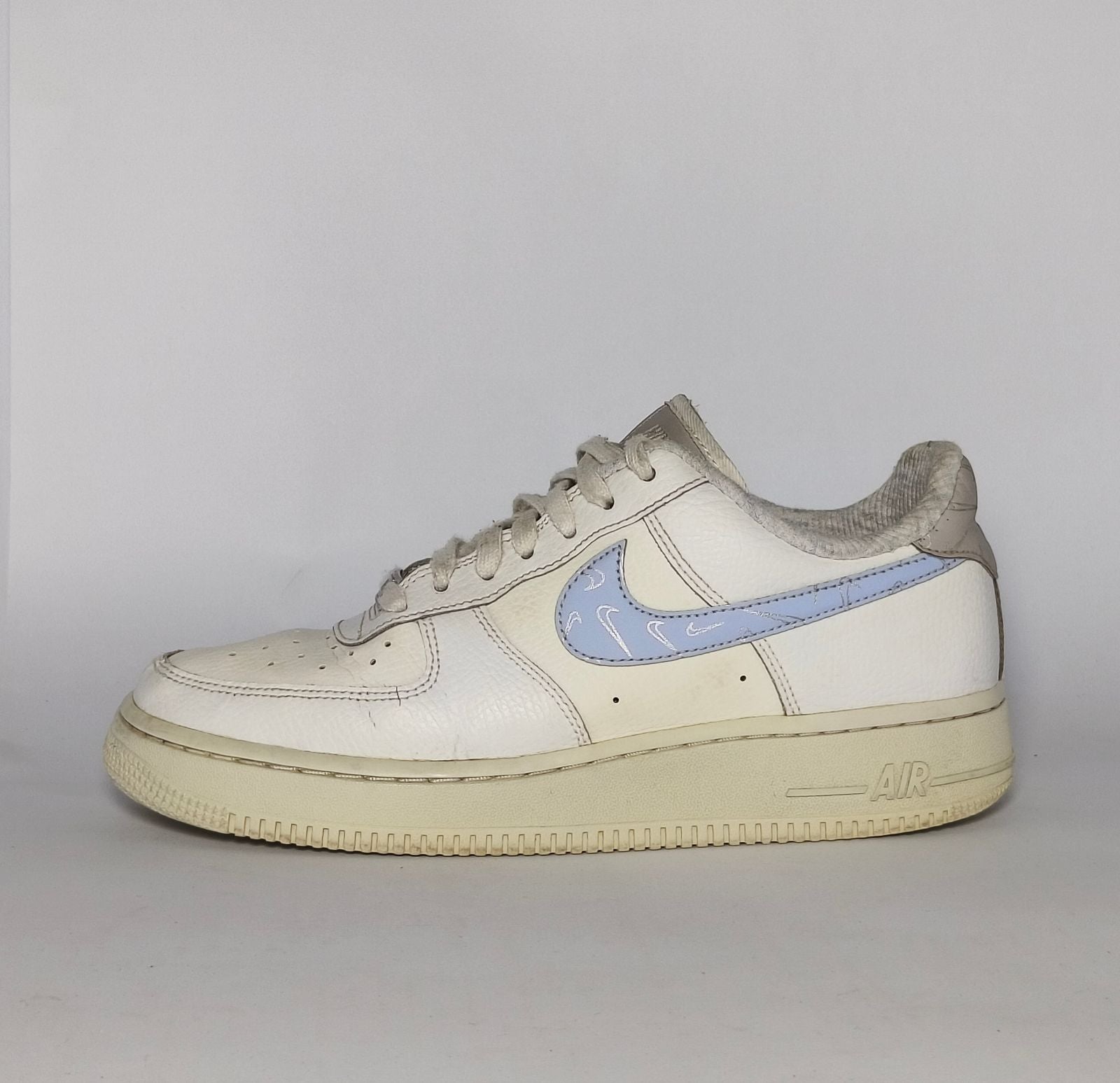 white Nike Air Force 1 Low sneaker featuring a light blue patterned Swoosh and a vintage sail-colored midsole.