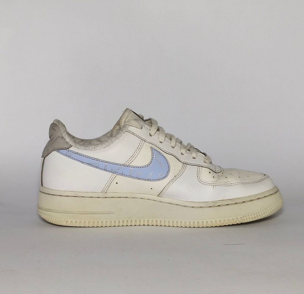 white Nike Air Force 1 Low sneaker featuring a light blue patterned Swoosh and a vintage sail-colored midsole.