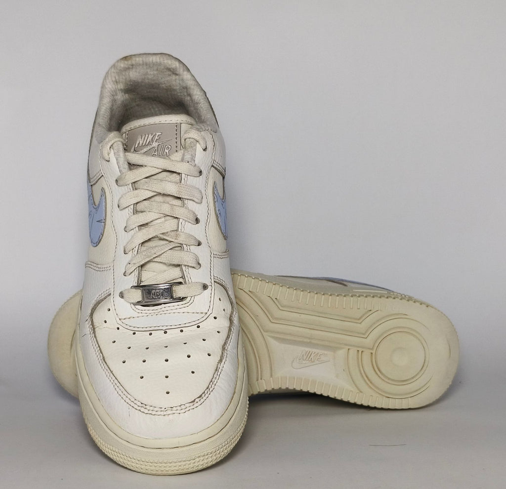 white Nike Air Force 1 Low sneaker featuring a light blue patterned Swoosh and a vintage sail-colored midsole.