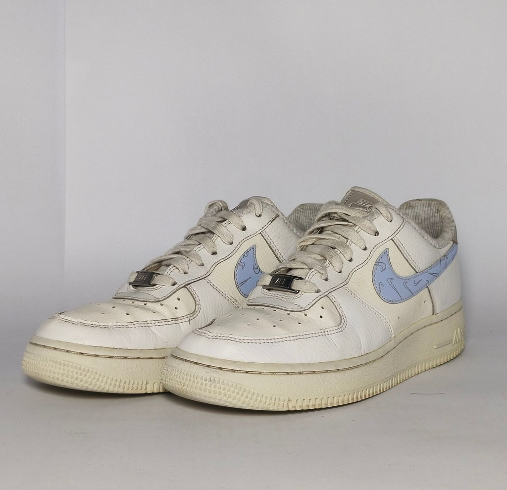 white Nike Air Force 1 Low sneaker featuring a light blue patterned Swoosh and a vintage sail-colored midsole.