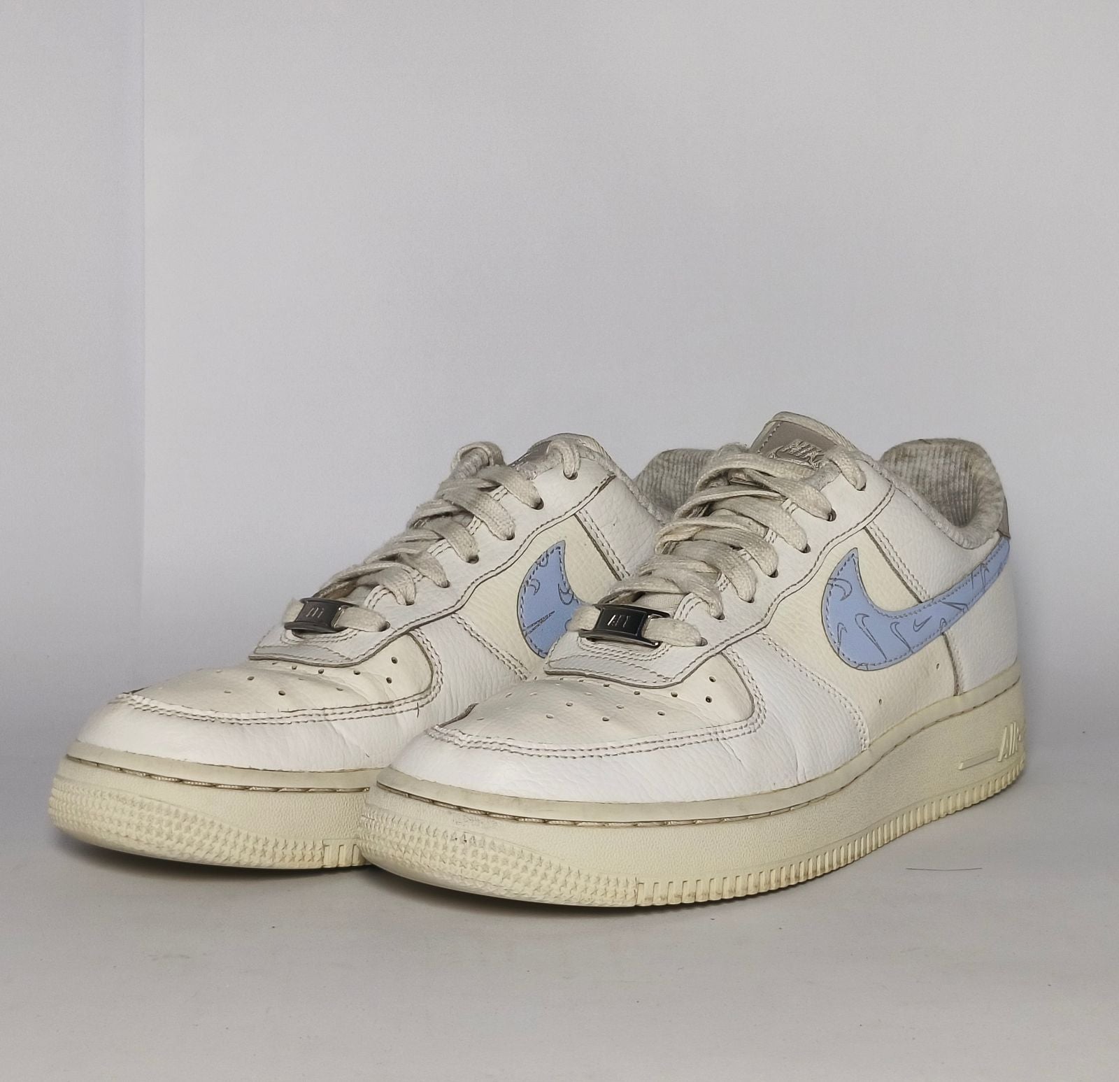 white Nike Air Force 1 Low sneaker featuring a light blue patterned Swoosh and a vintage sail-colored midsole.