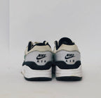 Nike Air Max 1 sneaker featuring a grey upper, black mudguard, and a green suede Swoosh with a visible air bubble in the white midsole.