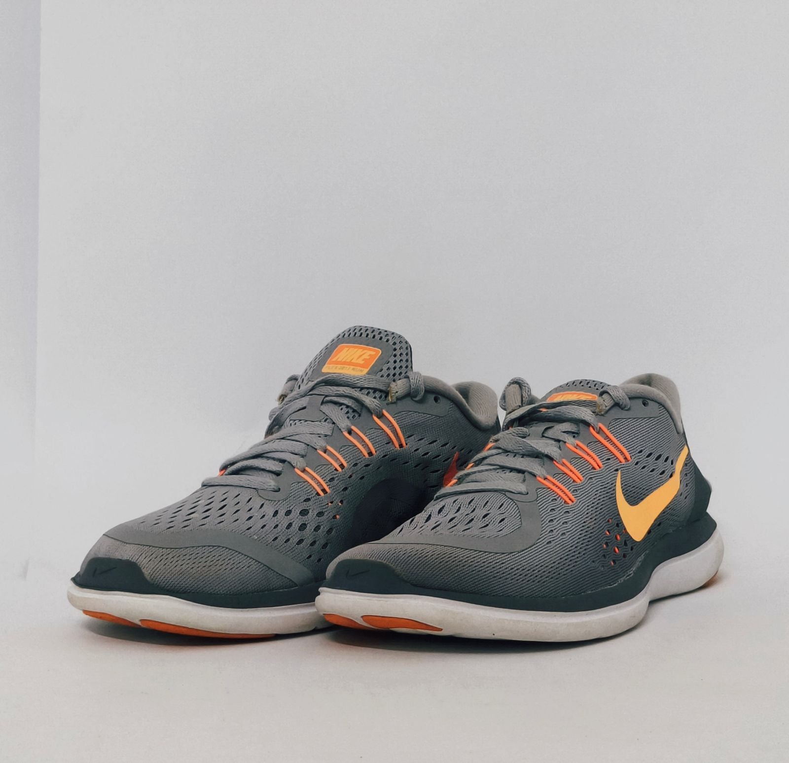 grey Nike Flex 2017 RN running shoe featuring an orange Swoosh and a flexible white midsole.