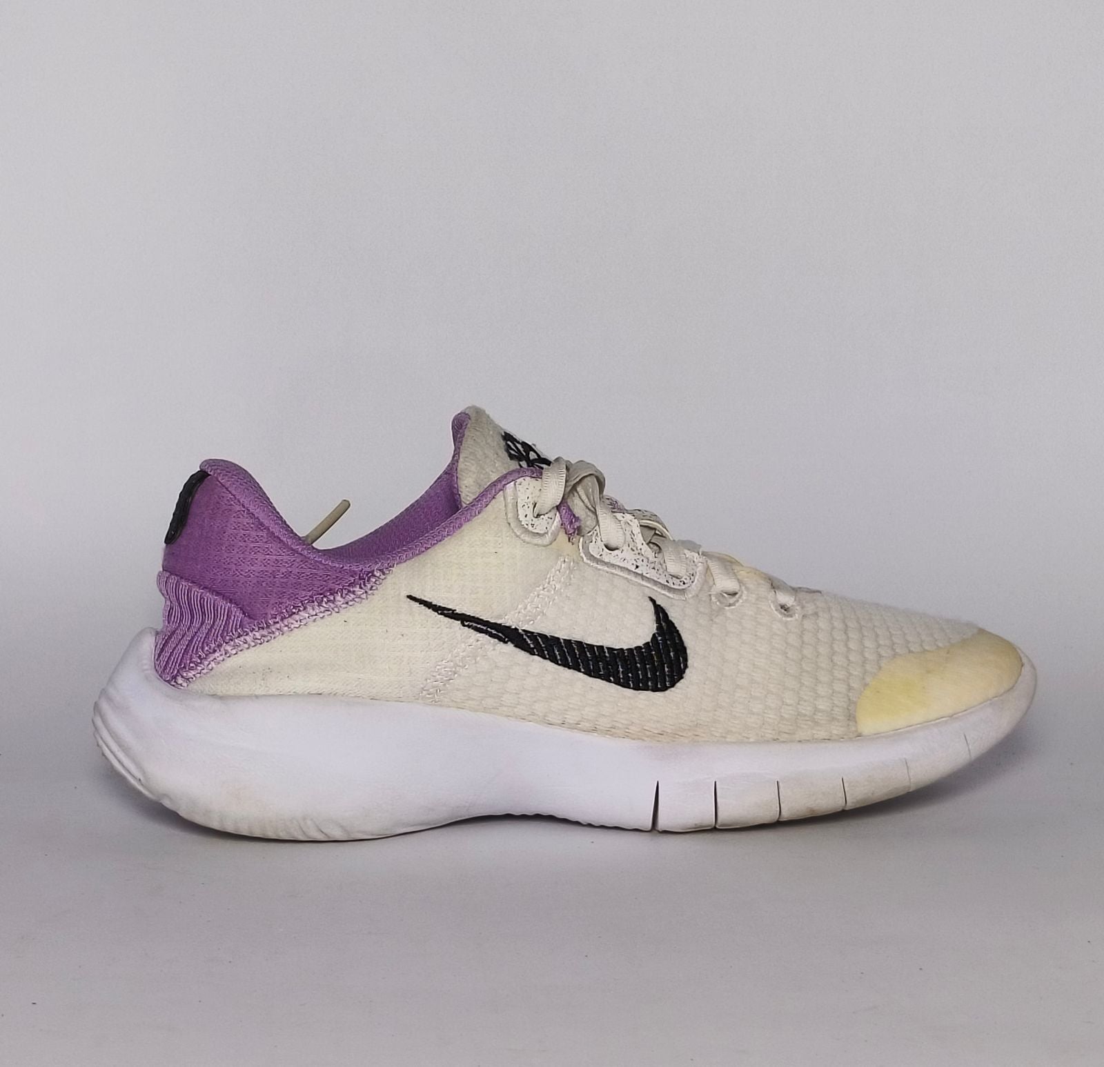 cream-colored Nike Flex Experience running shoe featuring a purple ankle collar, a black Swoosh, and a white flexible midsole.