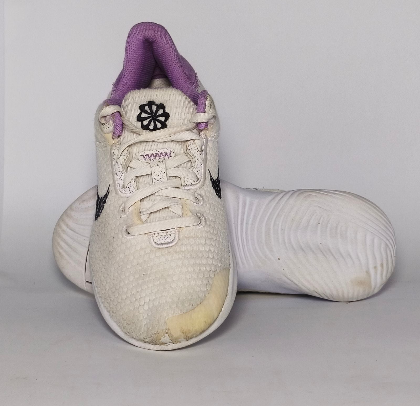 cream-colored Nike Flex Experience running shoe featuring a purple ankle collar, a black Swoosh, and a white flexible midsole.