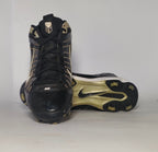 black Nike Huarache baseball cleat featuring a white Swoosh, gold heel accents, and a white midsole with a cleated outsole.