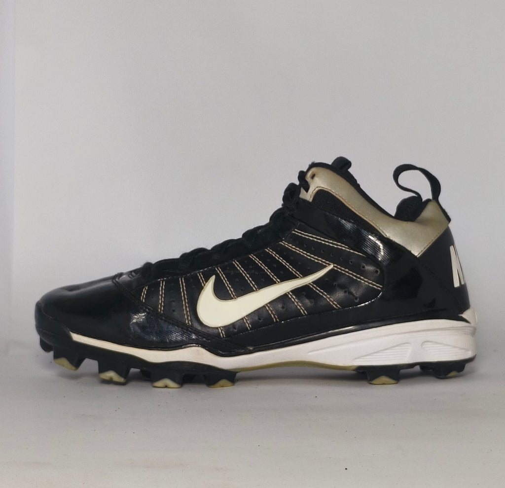 black Nike Huarache baseball cleat featuring a white Swoosh, gold heel accents, and a white midsole with a cleated outsole.
