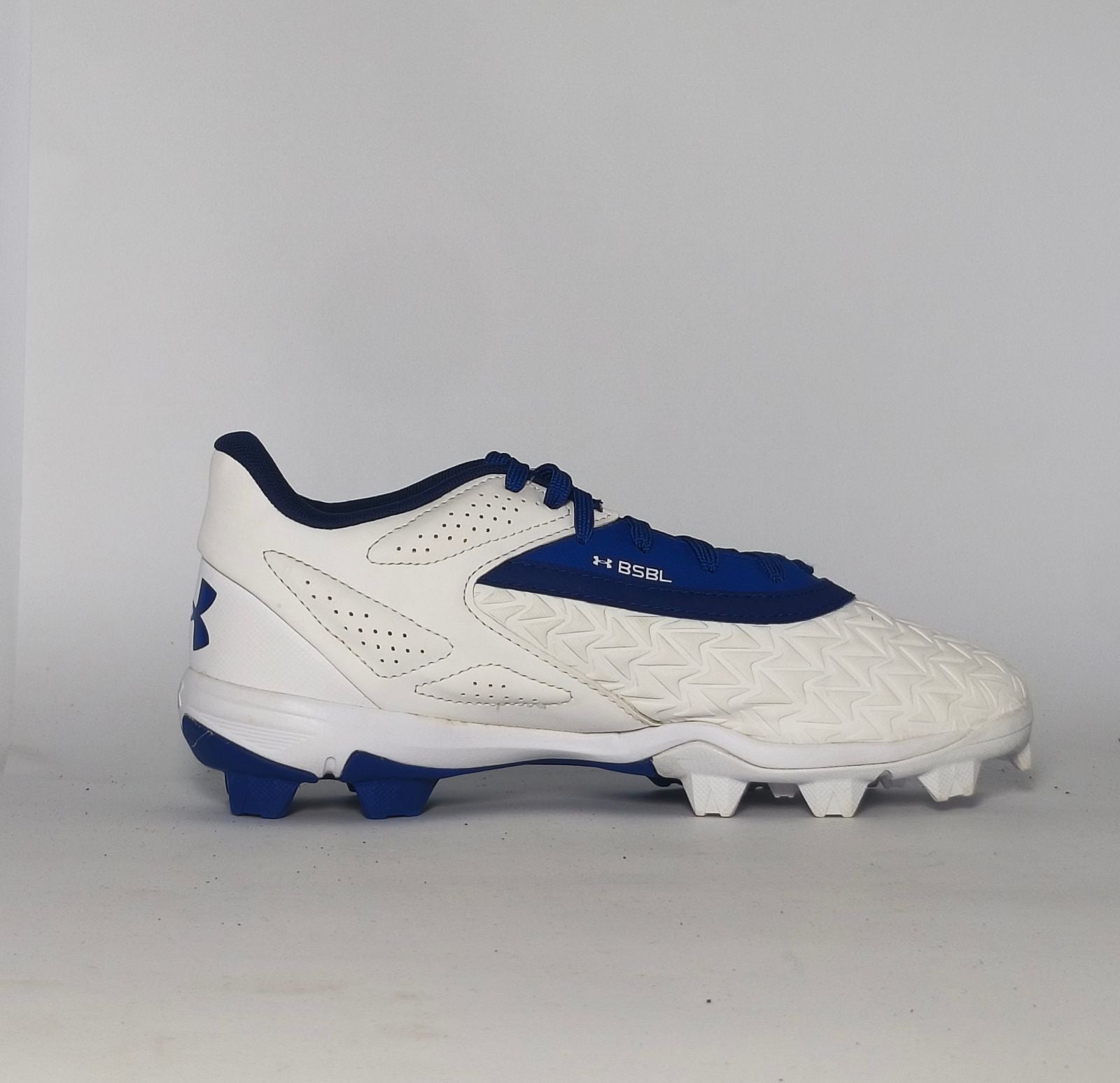 white and royal blue Under Armour cleat featuring a textured forefoot and a durable molded cleat outsole.