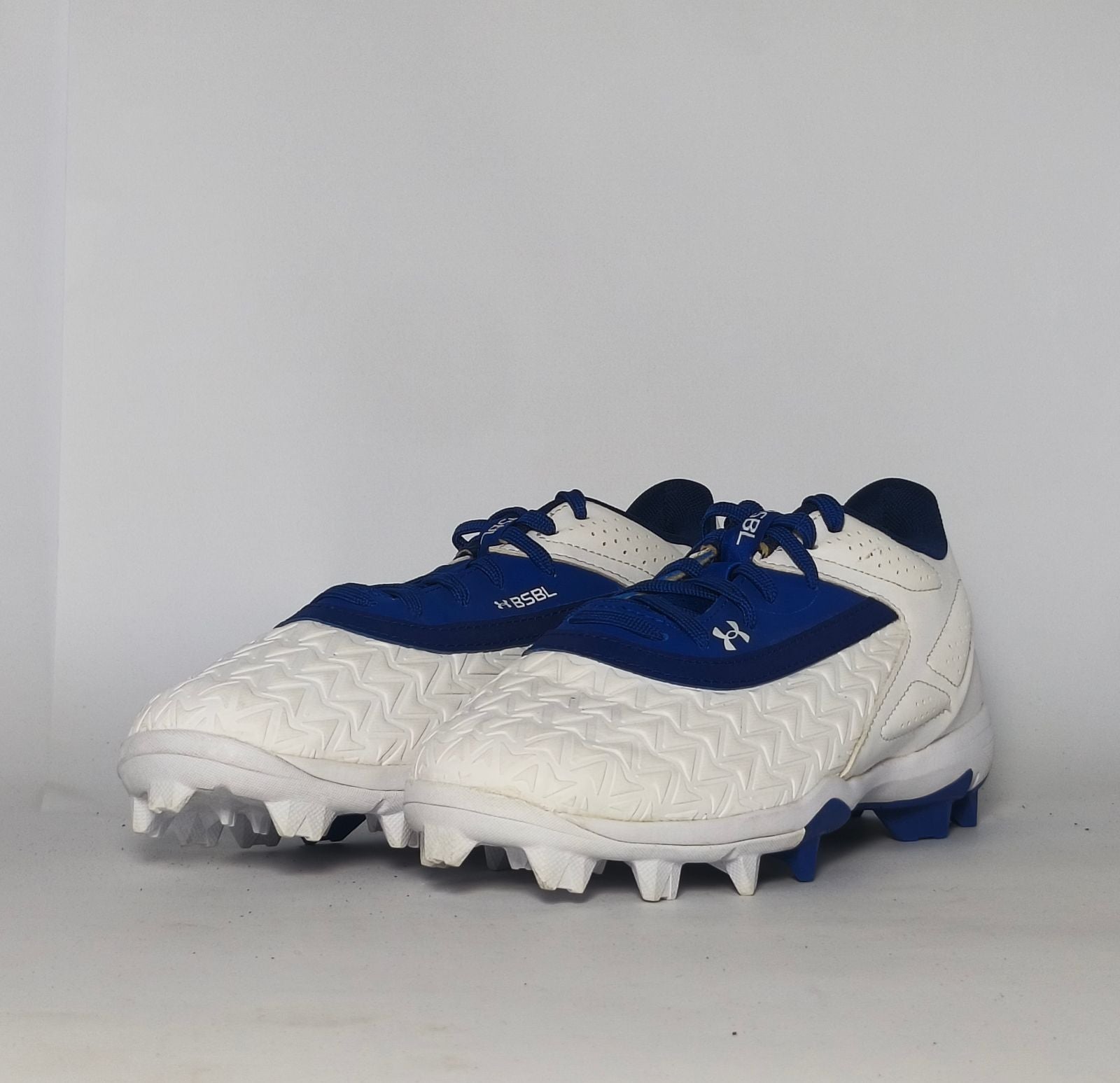 white and royal blue Under Armour cleat featuring a textured forefoot and a durable molded cleat outsole.