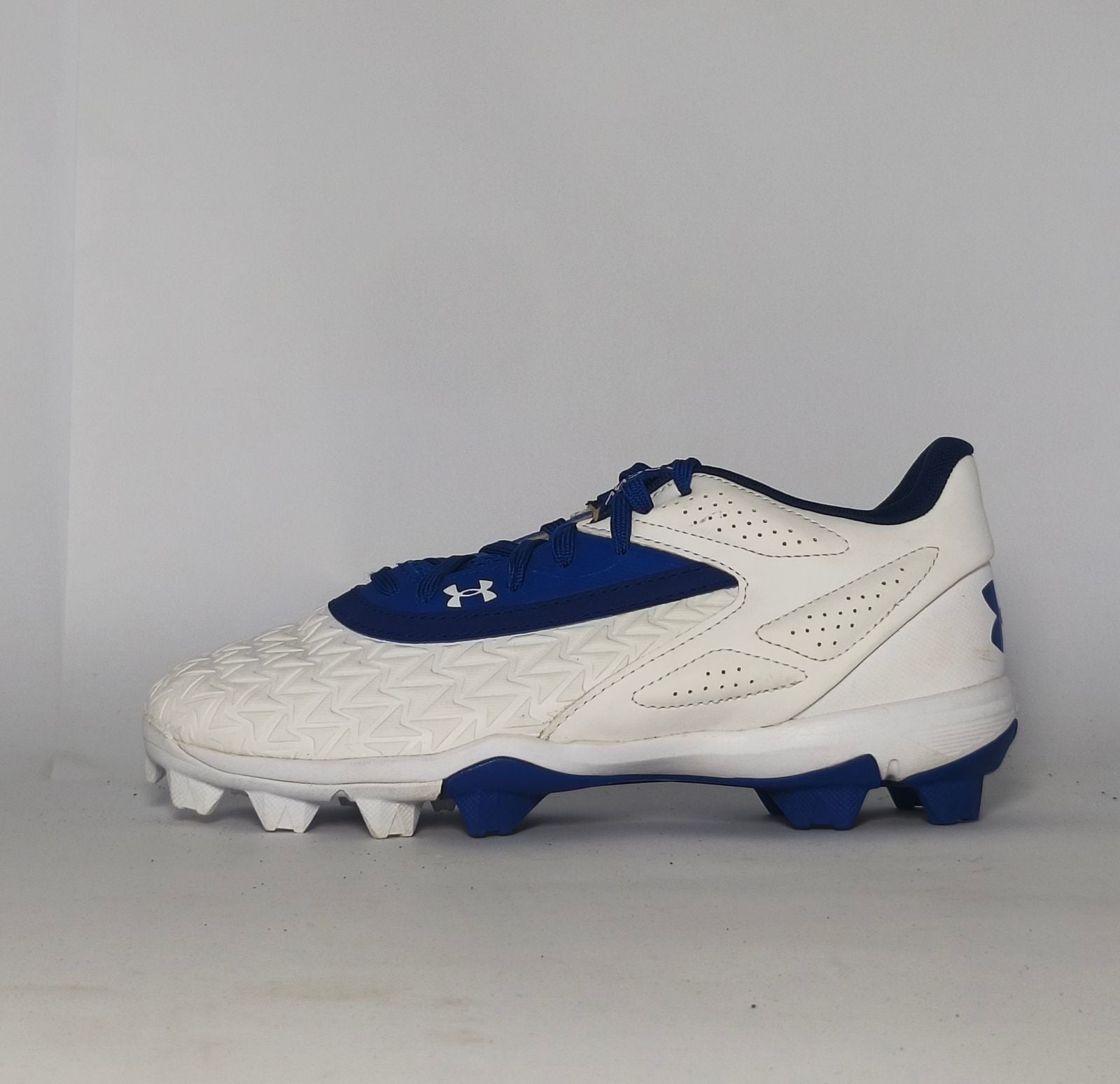 white and royal blue Under Armour cleat featuring a textured forefoot and a durable molded cleat outsole.